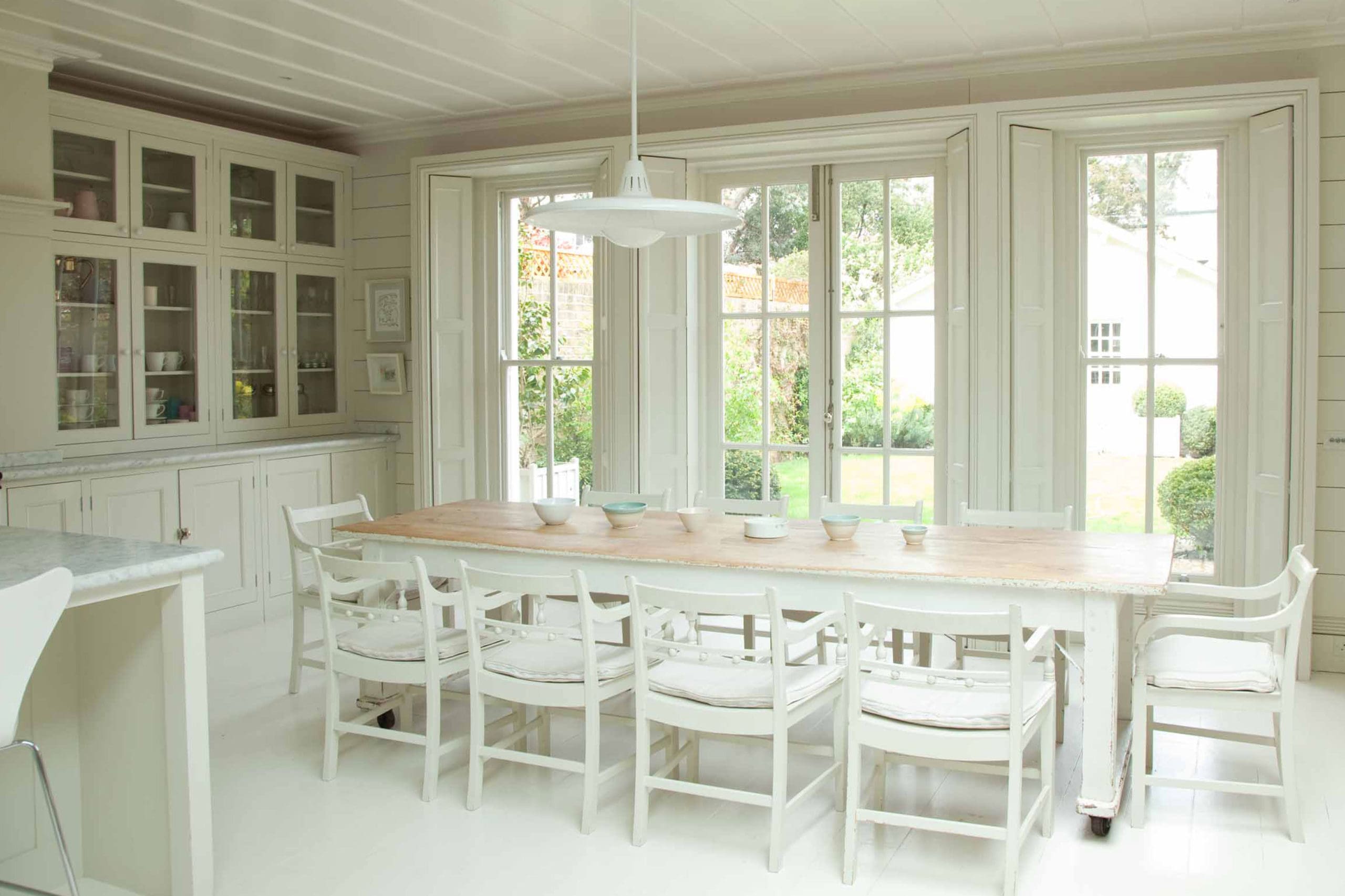  White country kitchen with long dinng table and glass wall cabinets
